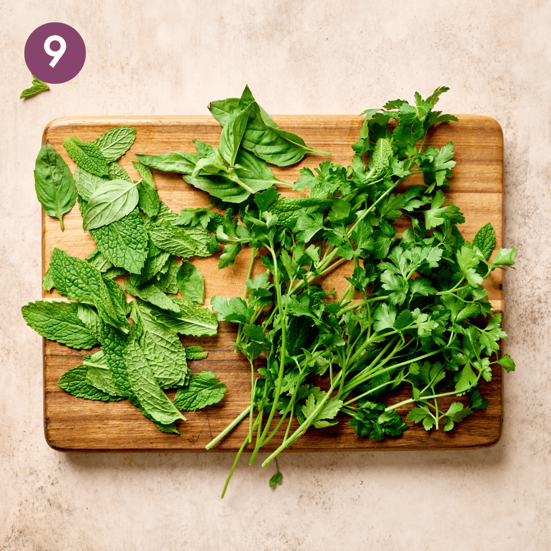 Fresh basil, mint and parsley on a wooden chopping board.