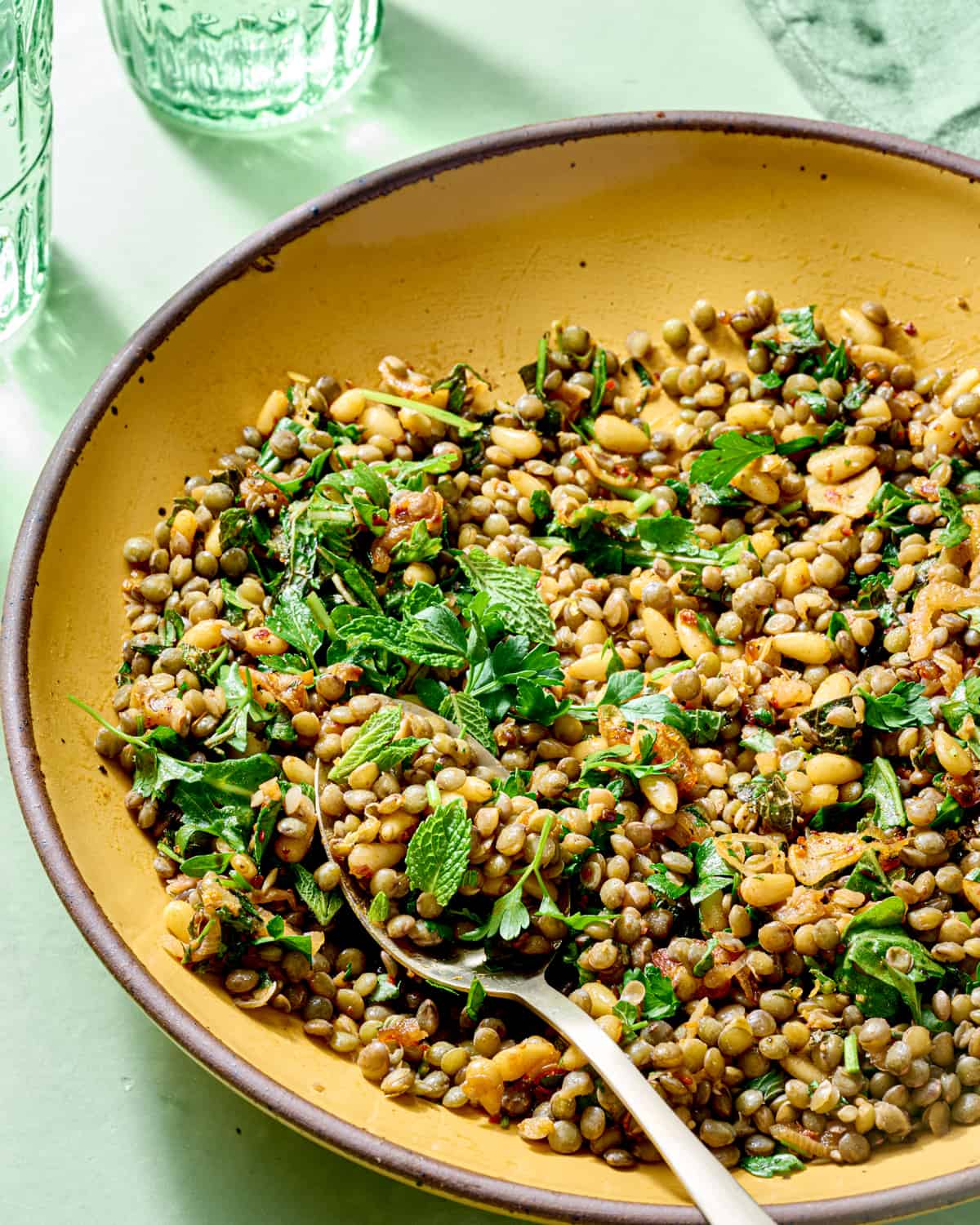 Side view of spoon in a yellow bowl with lentil salad and herbs.
