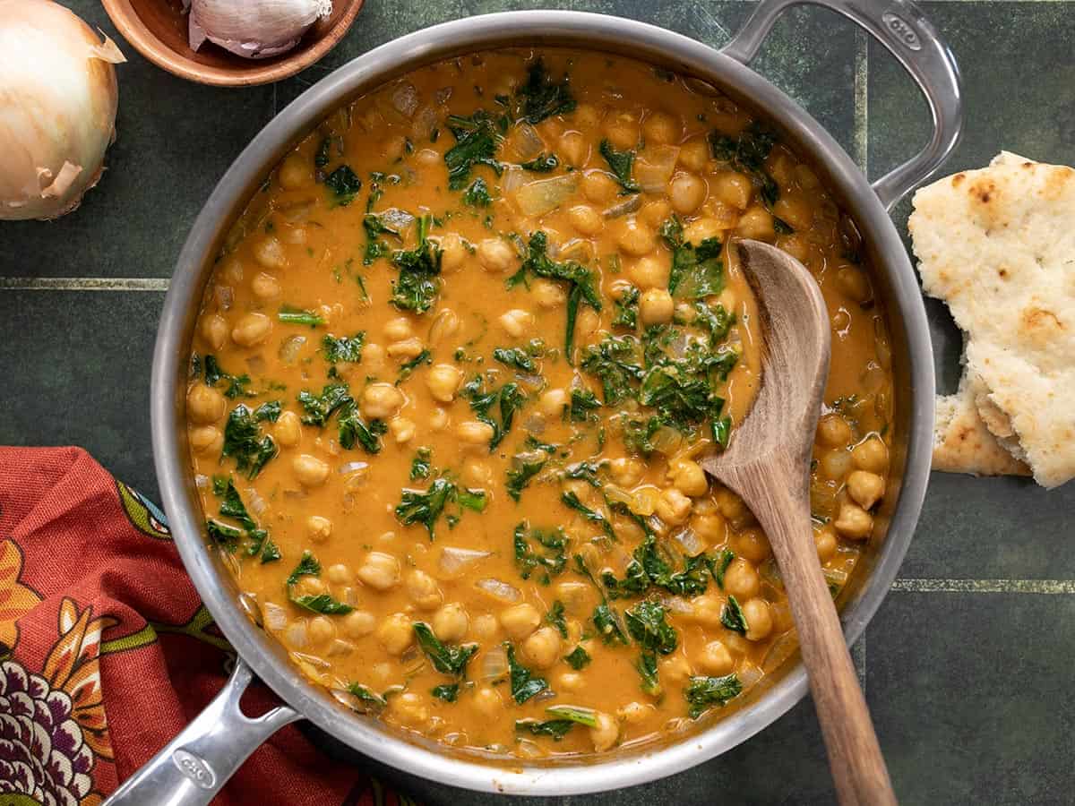 Overhead view of a skillet full of coconut curry chickpeas with a wooden spoon.