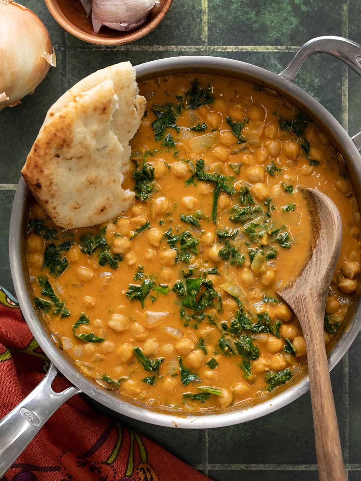 Finished skillet full of coconut curry chickpeas with naan and a wooden spoon.