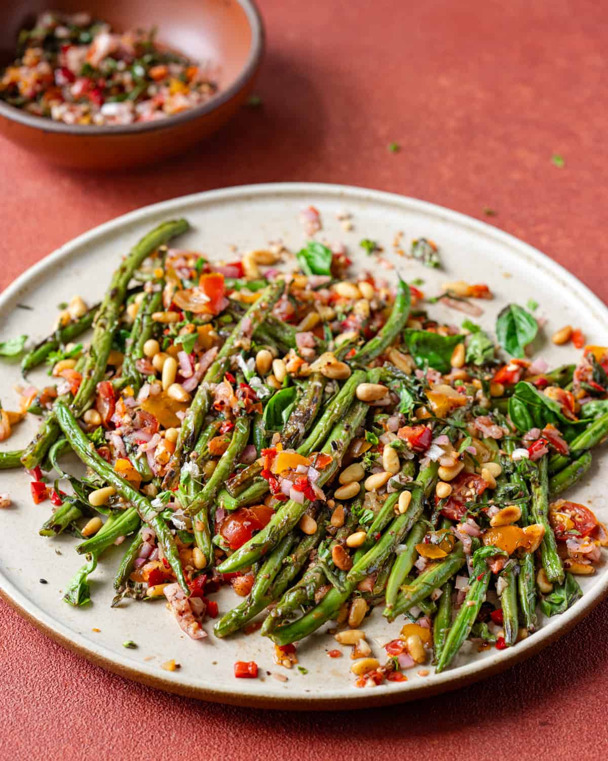 Side view of plate of charred green beans on a red table.