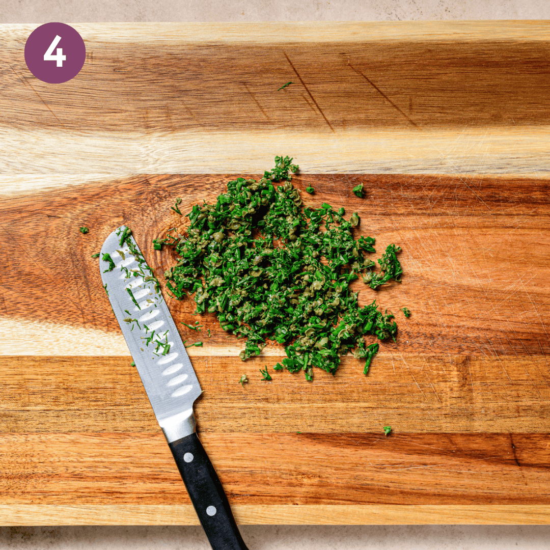 chopped herbs and a knife on a wooden cutting board.