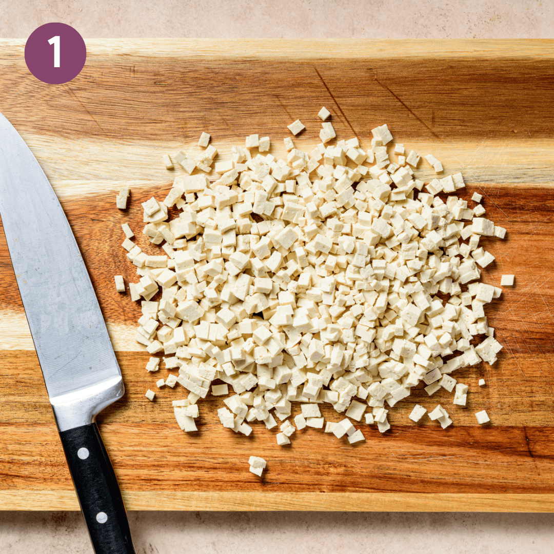 tofu cut into small pieces on a wooden cutting board.