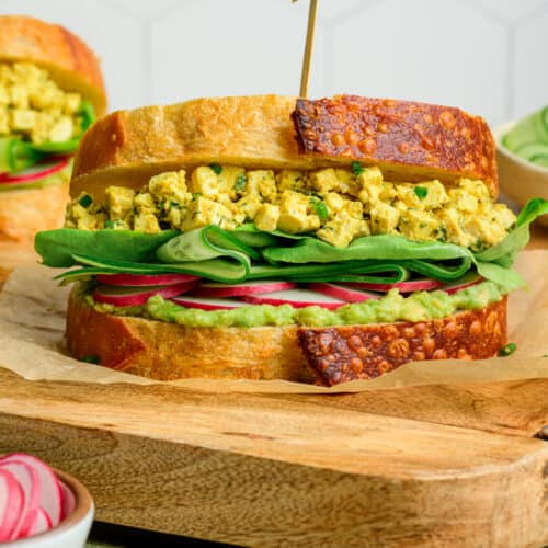 side view of egg salad sandwich on a wooden cutting board.