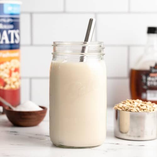 A jar of homemade oat milk with a metal straw and ingredients on the sides.