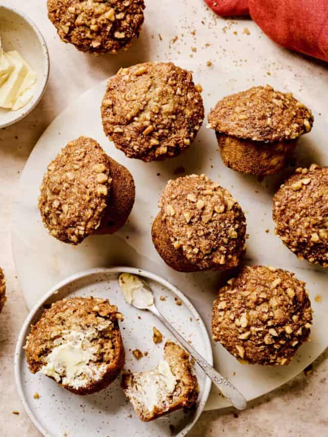 Baked banana muffins on a serving platter with one muffin sliced open and buttered.