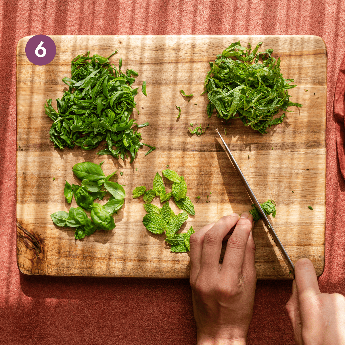 thinly sliced basil and mint on a cutting board with woman's hands slicing mint leaves.