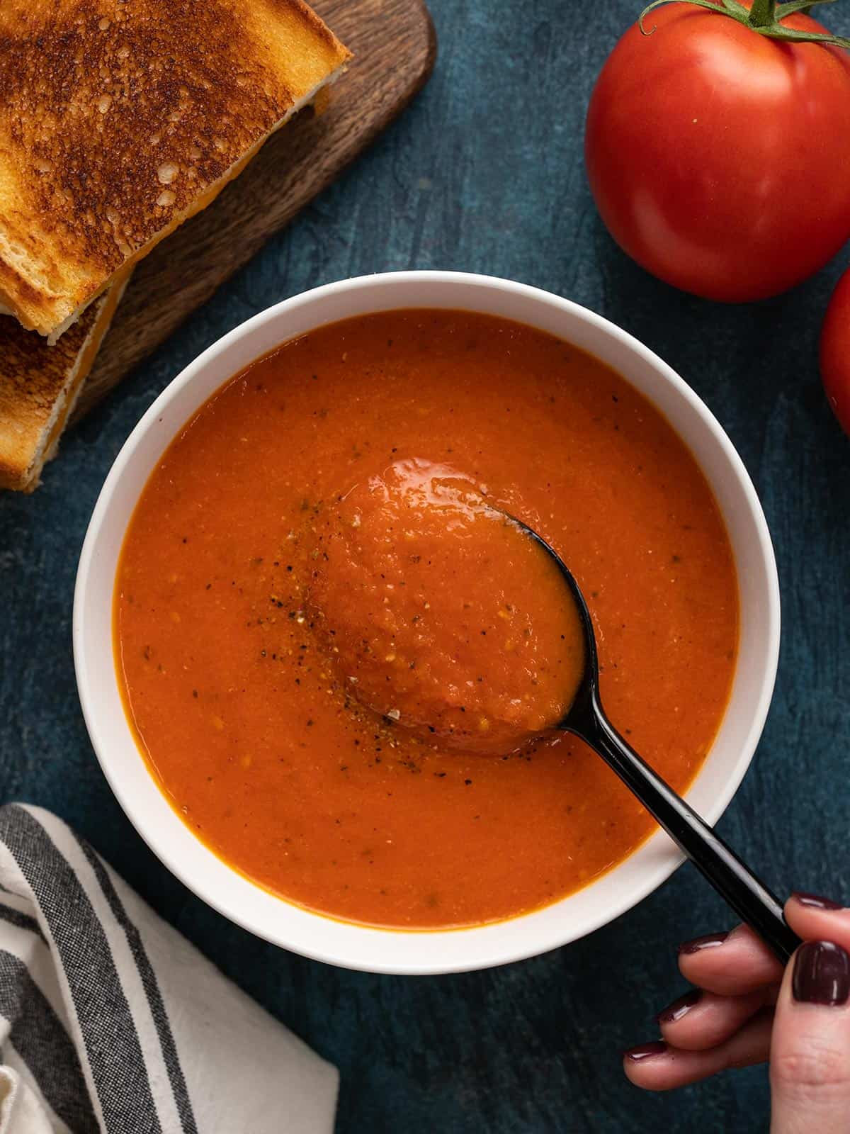 Overhead view of a bowl of roasted tomato soup with a spoon and grilled cheese on the side.