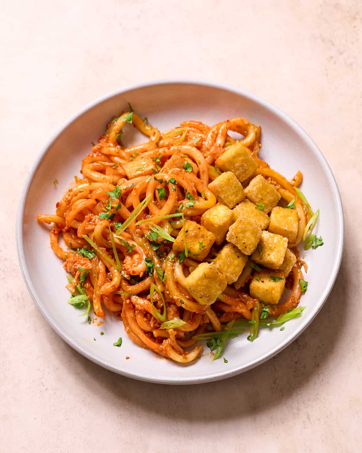 side view of Baked tofu and noodles with herbs in a bowl on a table.