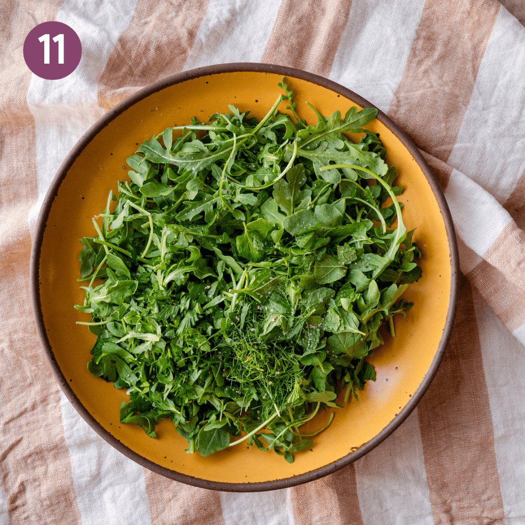 A large bowl of arugula topped with parsley, salt and pepper on a table.