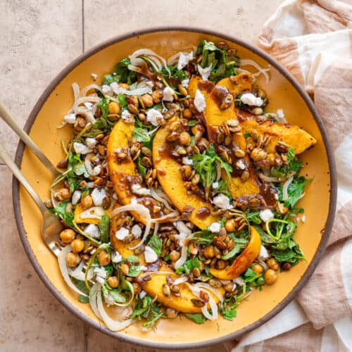 Pumpkin salad on a yellow plate next to a linen napkin on a tan table.