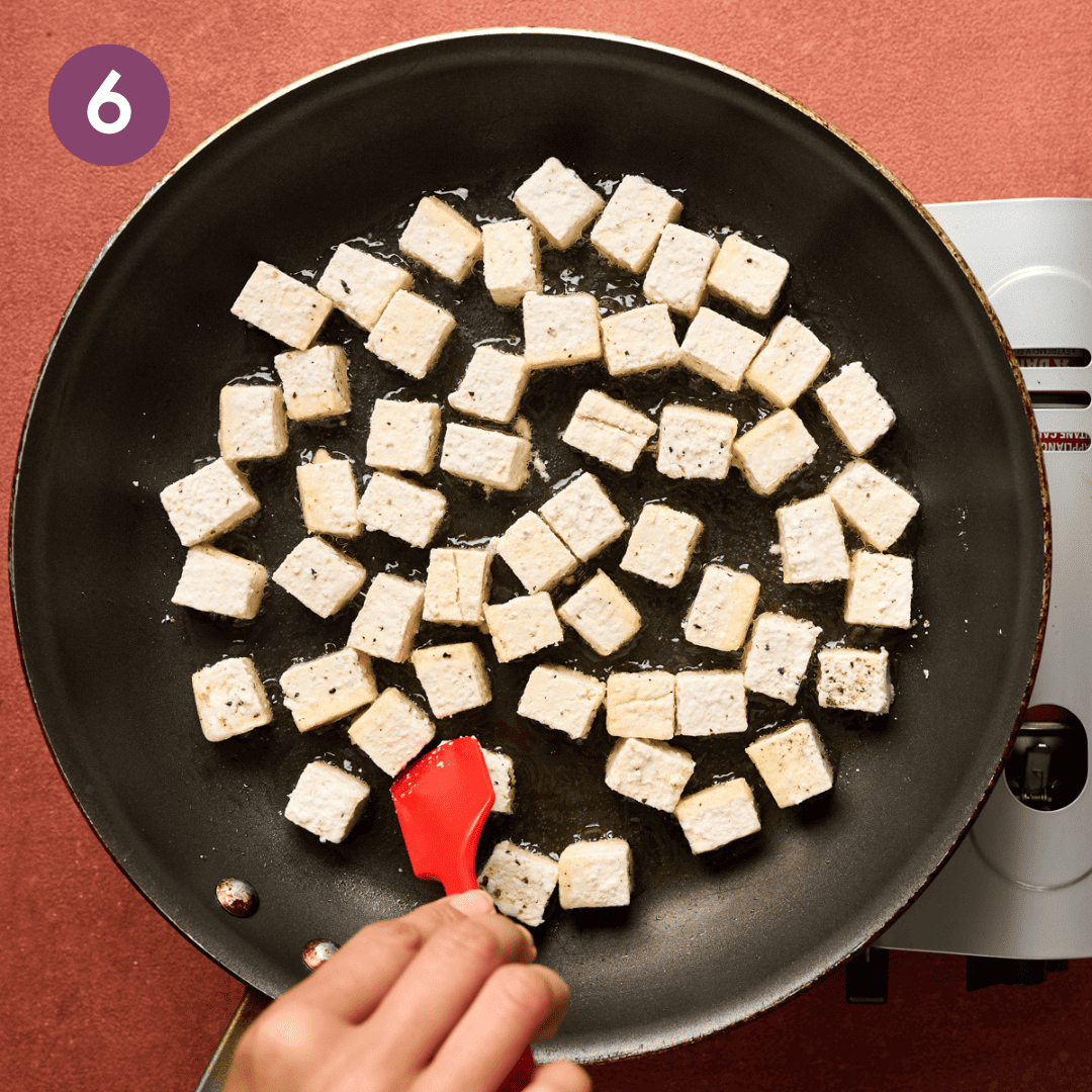Person flipping tofu cubes in the pan with a silicone spatula.