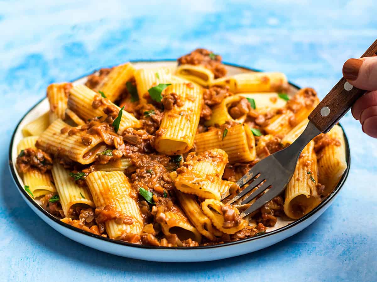 Side view of a plate full of pasta and lentil bolognese with a fork in the side.