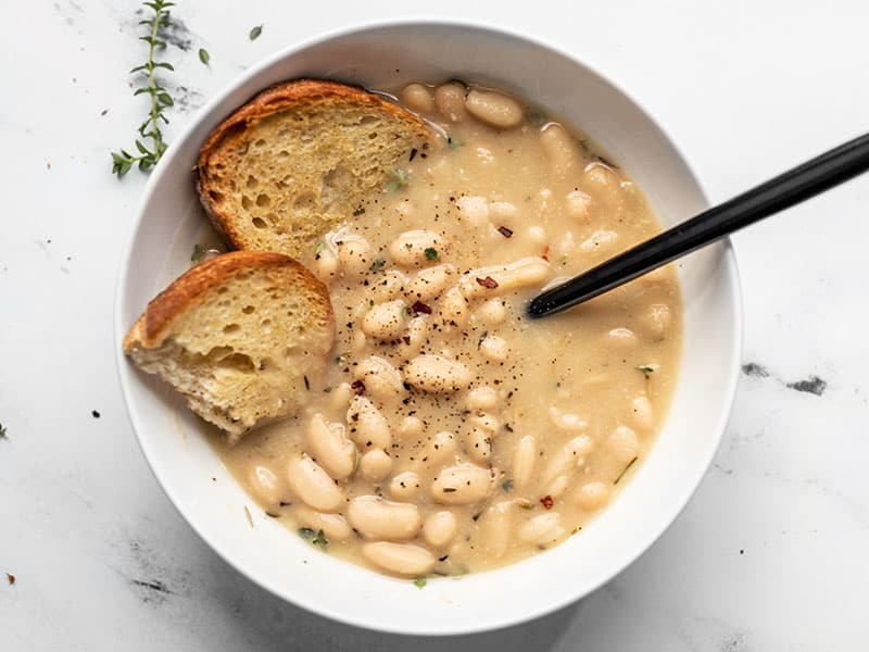 A bowl of Rosemary Garlic White Bean Soup with two pieces of toasted bread and a black spoon in the middle.