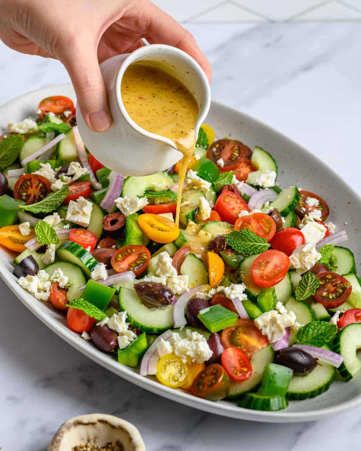 person pouring red wine vinaigrette over a platter of salad.