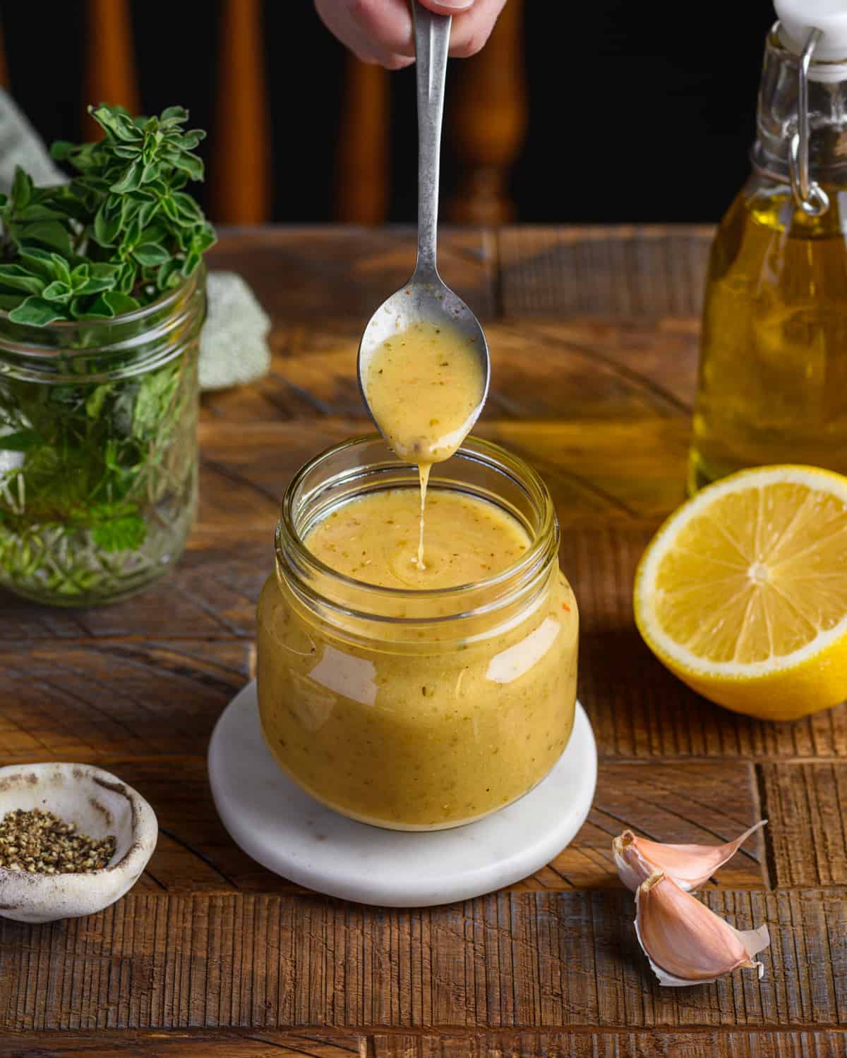 person taking a spoon from a glass jar of vinaigrette on a wooden table.